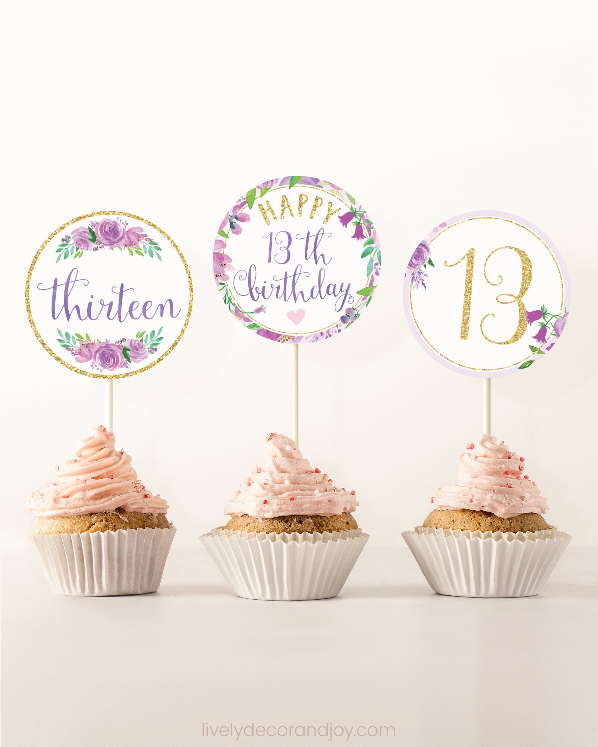 Three cupcakes side by side. Each has a round cupcake topper with purple watercolor flowers and purple and gold letters.