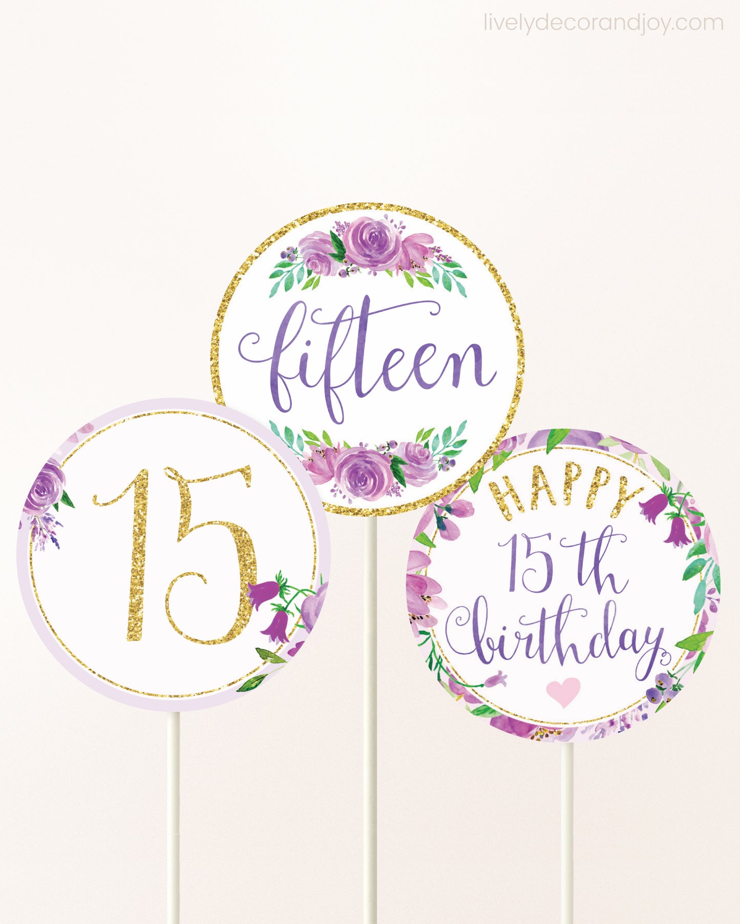 Three cupcakes toppers attached to lollipop sticks. They feature purple watercolor floral designs and purple and gold handwritten text.