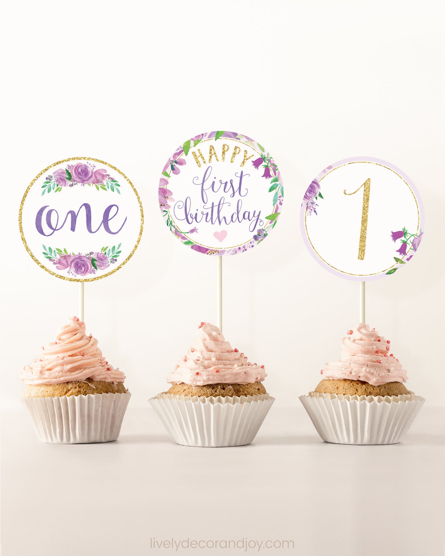 Three cupcakes side by side. Each has a round cupcake topper with purple watercolor flowers and purple and gold letters.