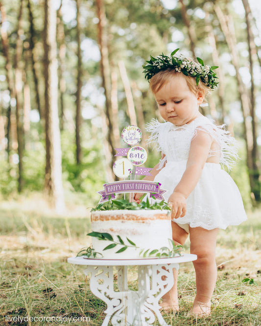 A cute little girl next to her healthy smash cake in a park. It is a rustic sponge cake with a printed cake topper.