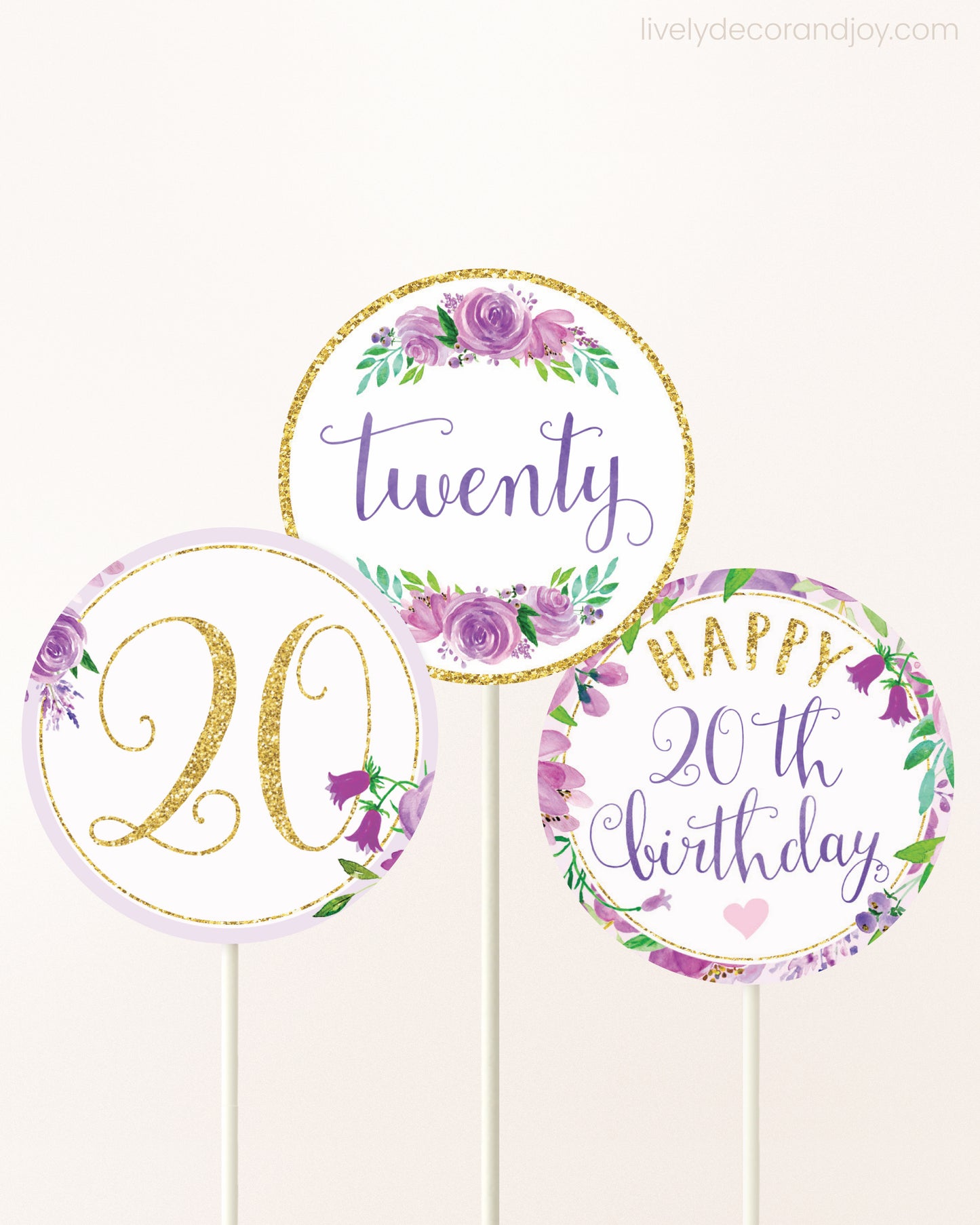 Three cupcakes toppers attached to lollipop sticks. They feature purple watercolor floral designs and purple and gold handwritten text.