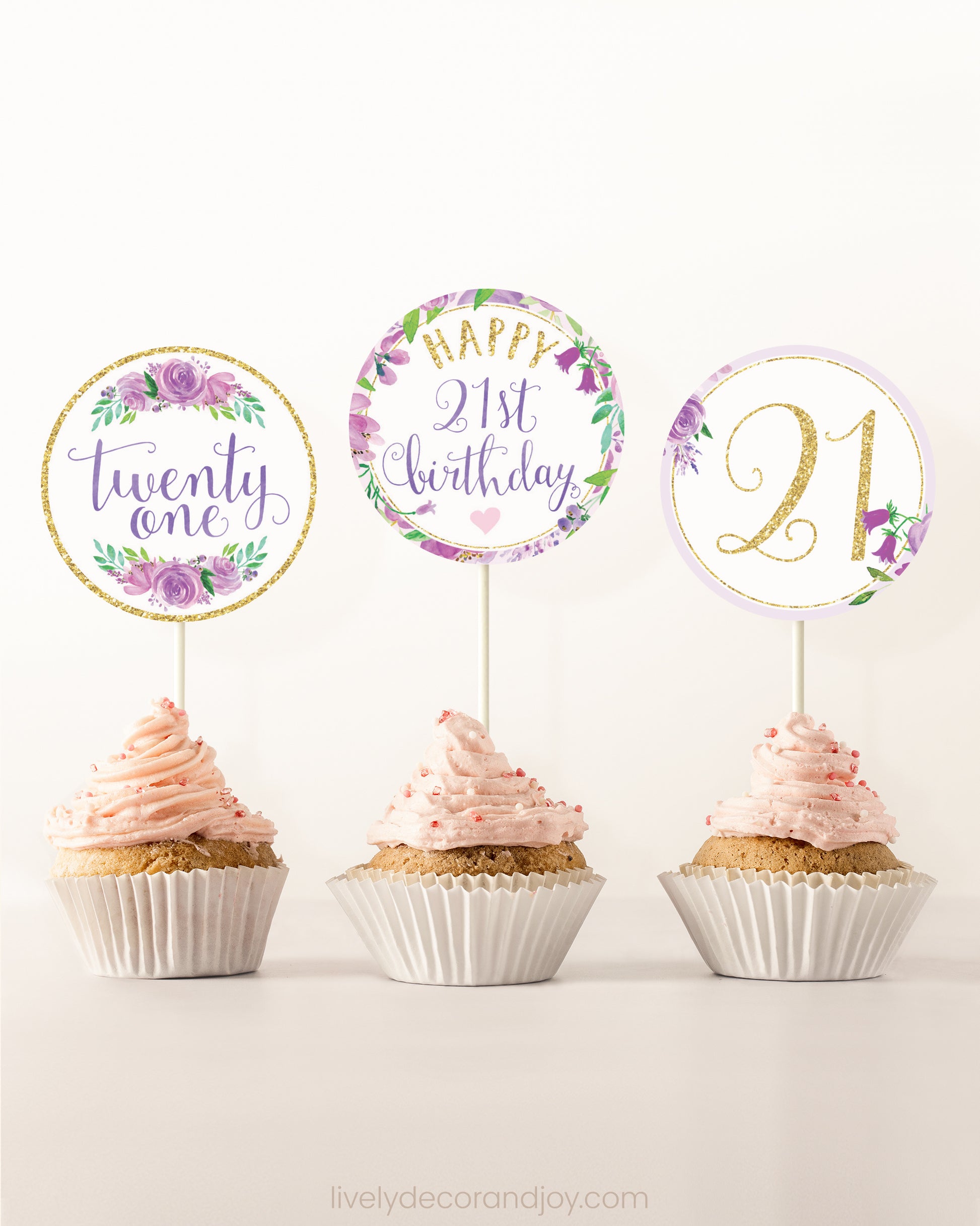 Three cupcakes side by side. Each has a round cupcake topper with purple watercolor flowers and purple and gold letters.