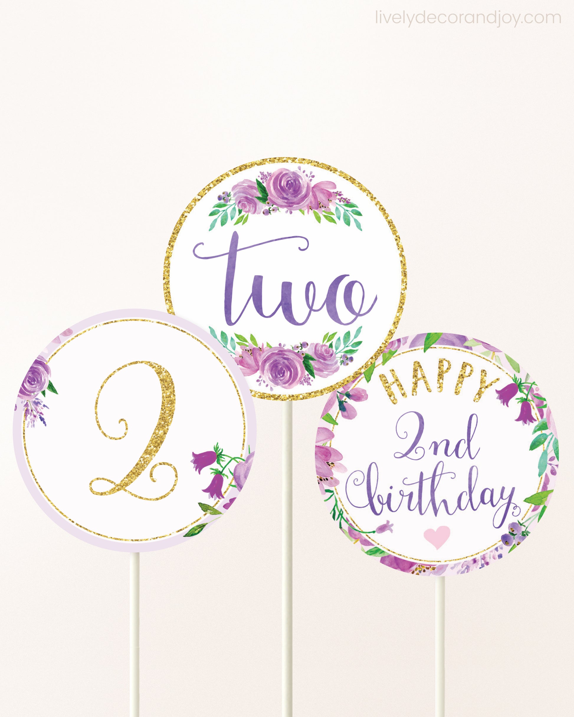 Three cupcakes toppers attached to lollipop sticks. They feature purple watercolor floral designs and purple and gold handwritten text.