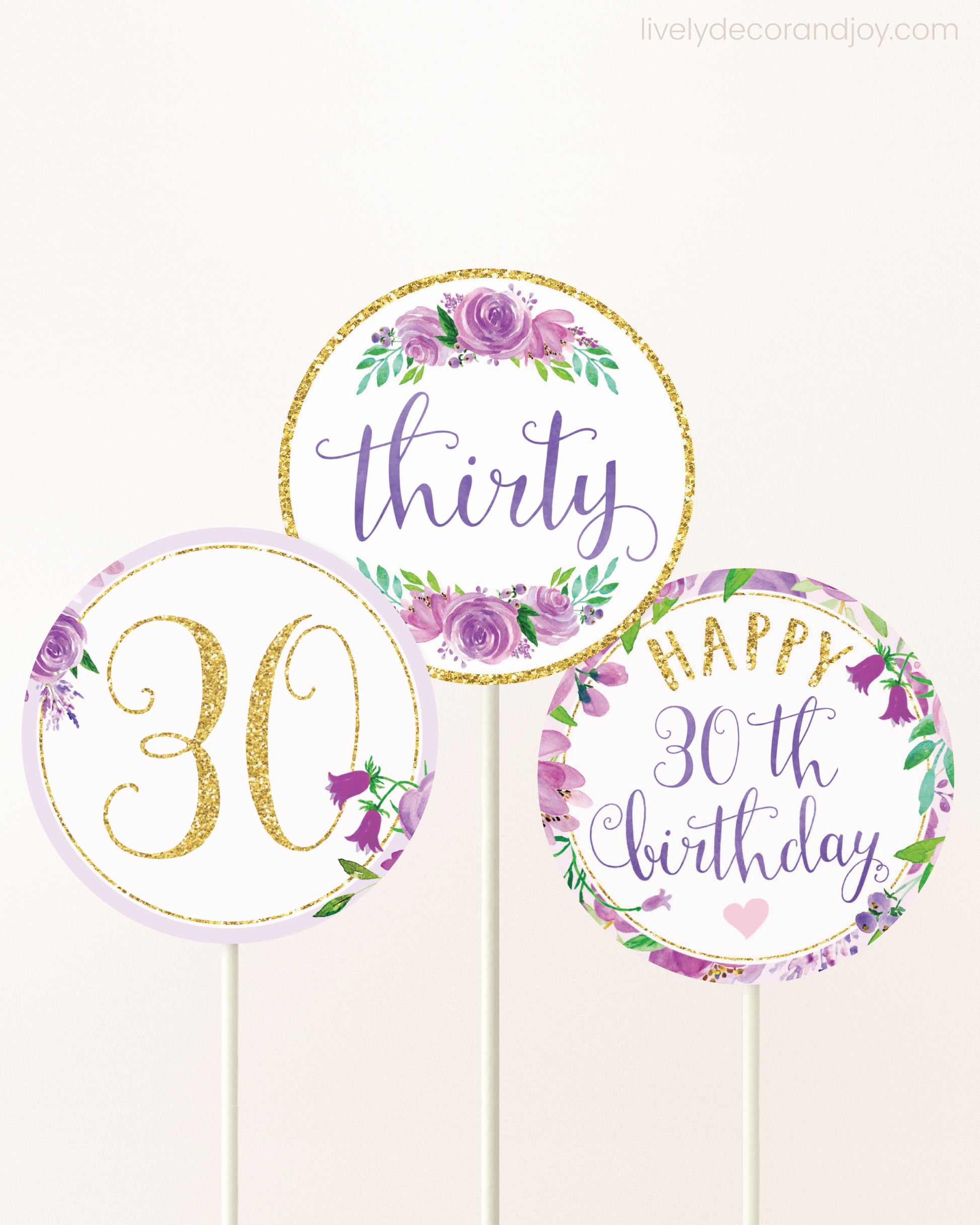 Three cupcakes toppers attached to lollipop sticks. They feature purple watercolor floral designs and purple and gold handwritten text.