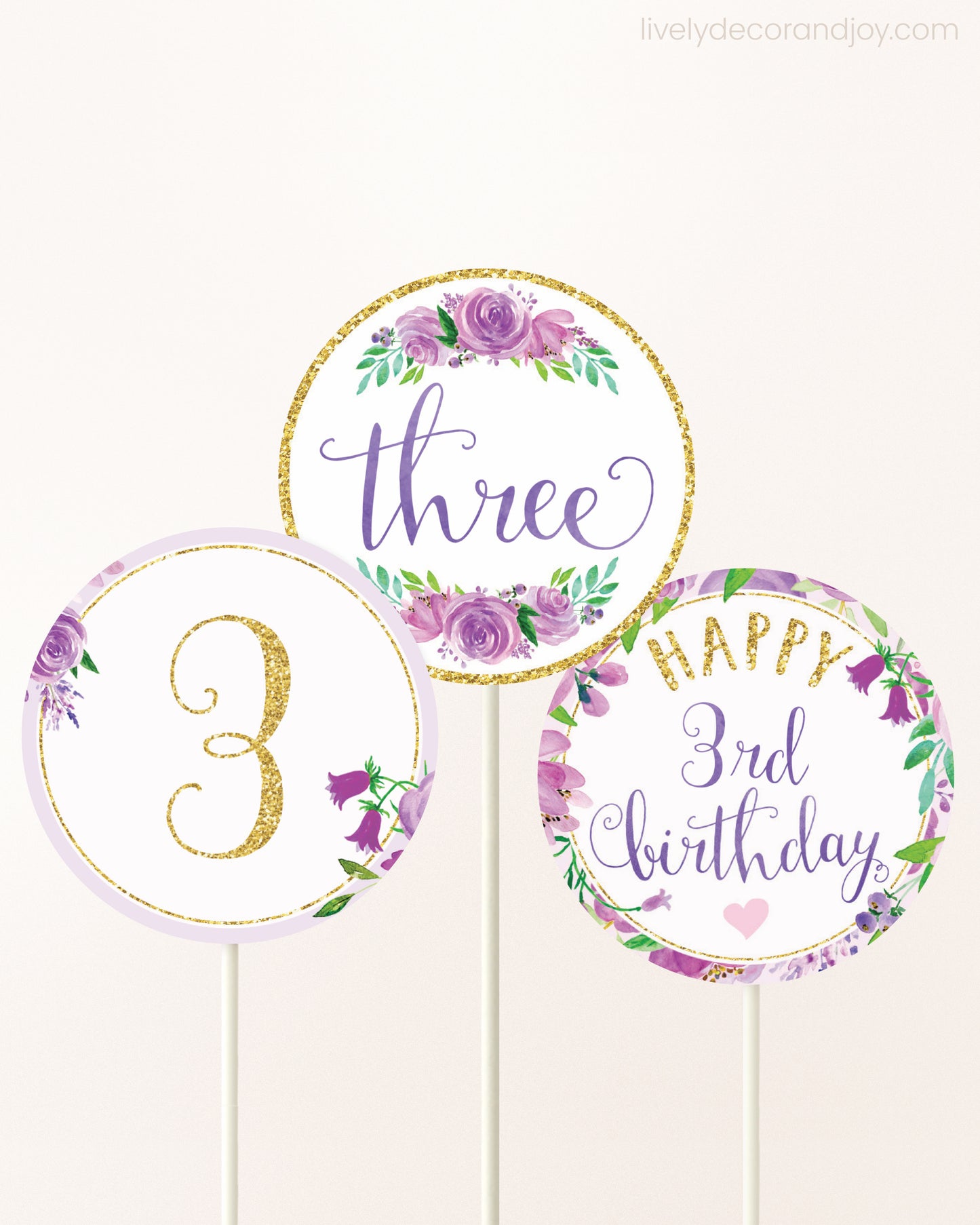 Three DIY toppers attached to lollipop sticks. They show printable cupcake topper designs with purple watercolor flowers.