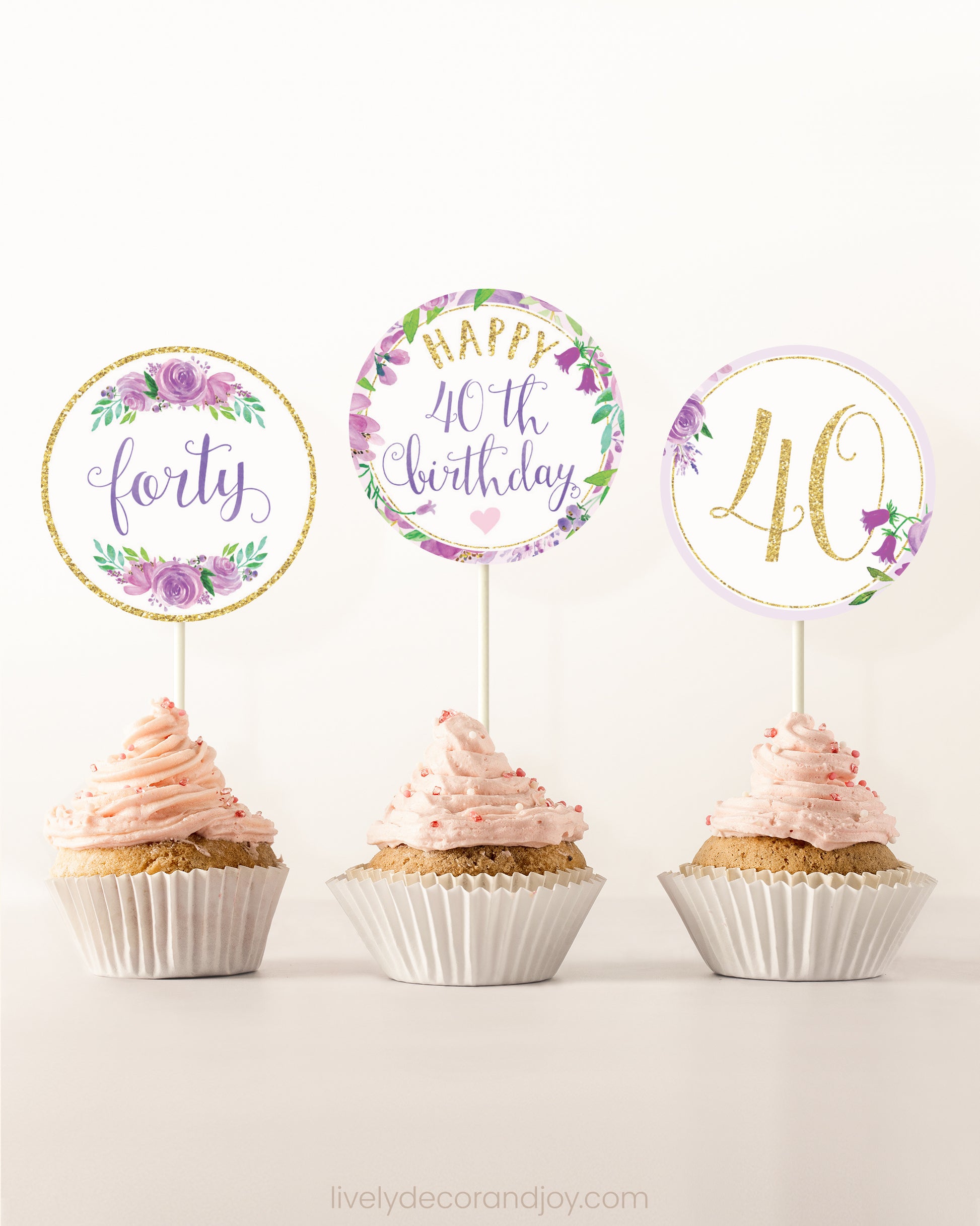 Three cupcakes side by side. Each has a round cupcake topper with purple watercolor flowers and purple and gold letters.