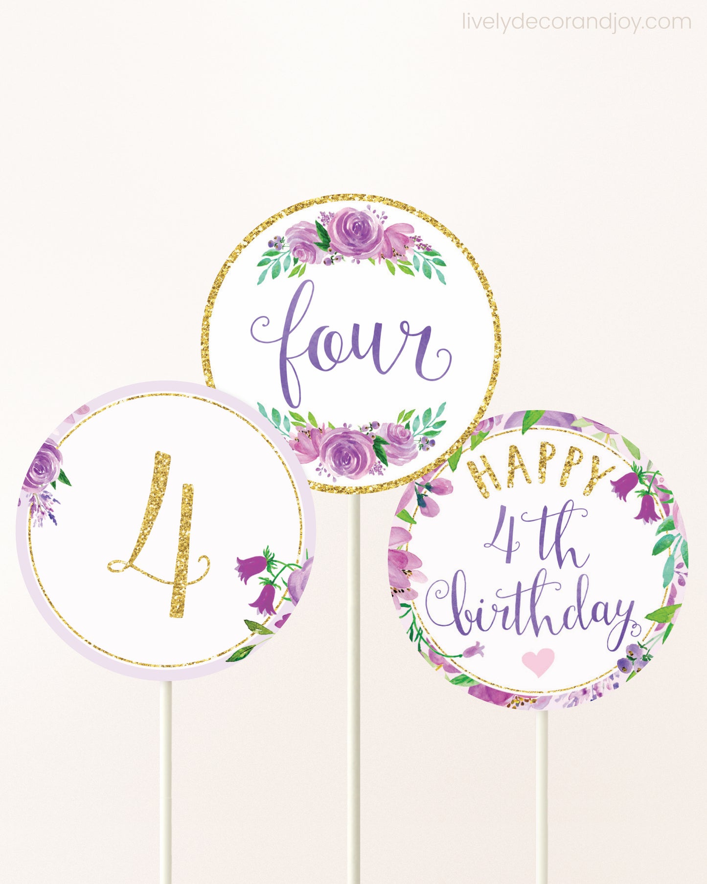 Three cupcakes toppers attached to lollipop sticks. They feature purple watercolor floral designs and purple and gold handwritten text.