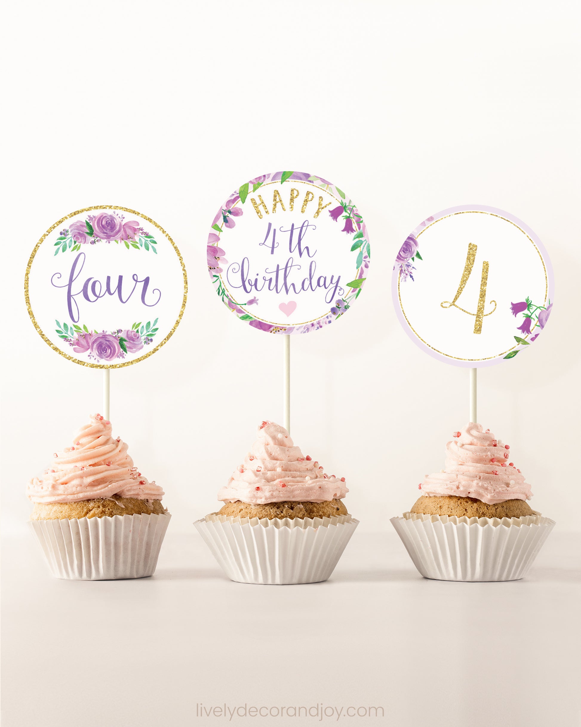 Three cupcakes on a dessert table. Each has a round cupcake topper with purple watercolor floral designs and purple and gold letters.