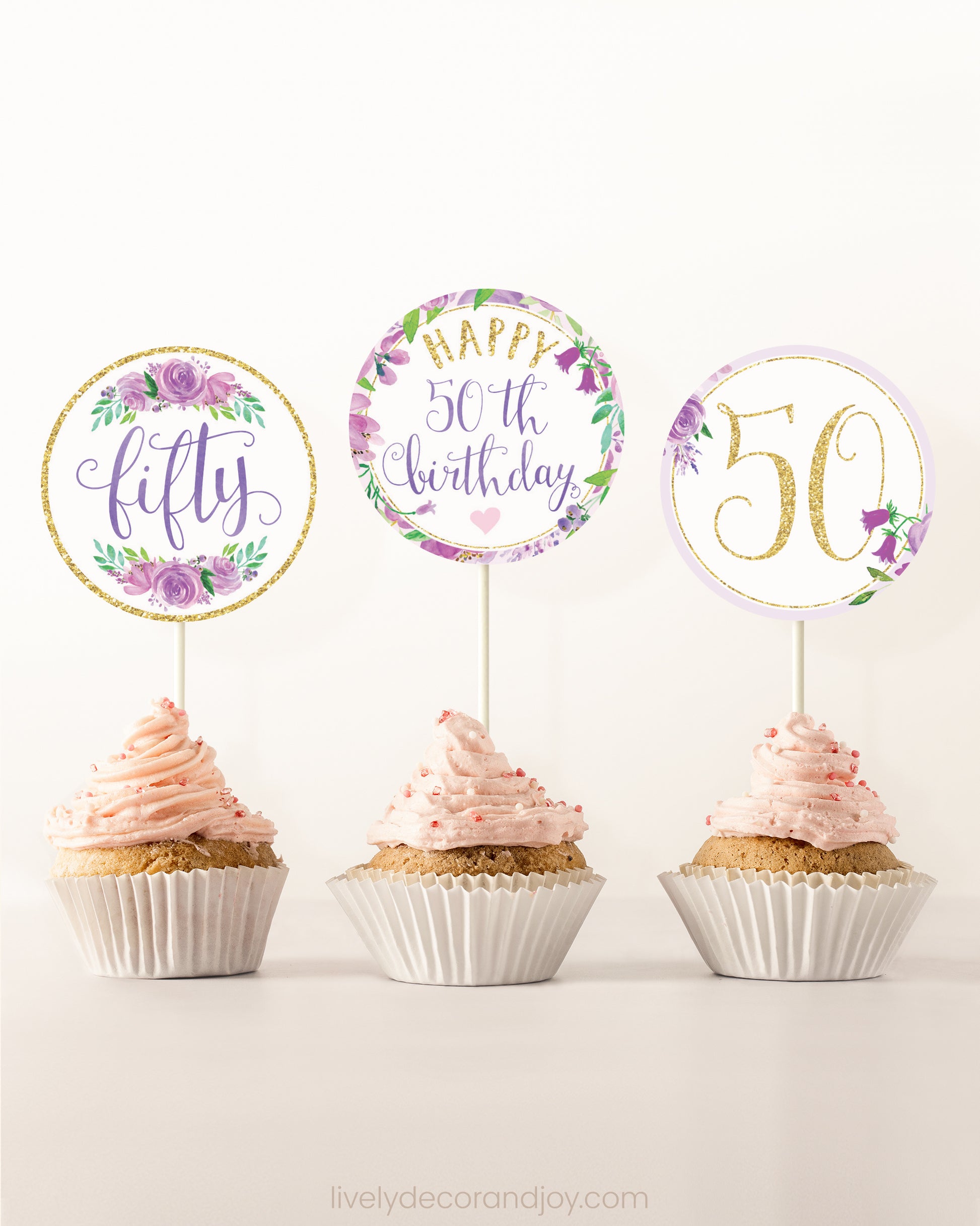 Three cupcakes side by side. Each has a round cupcake topper with purple watercolor flowers and purple and gold letters.