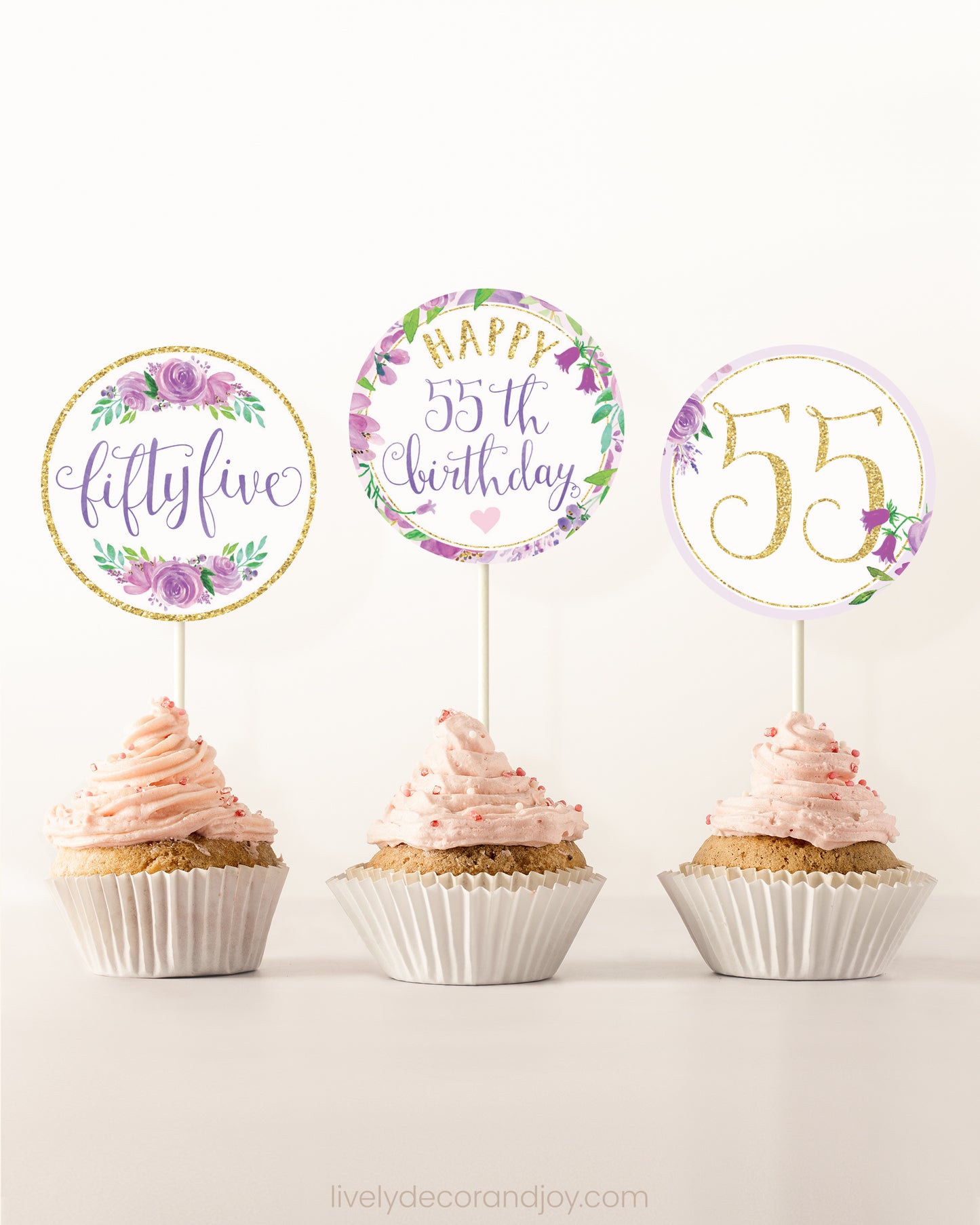 Three cupcakes on a dessert table. Each has a round cupcake topper with purple watercolor floral designs and purple and gold letters.