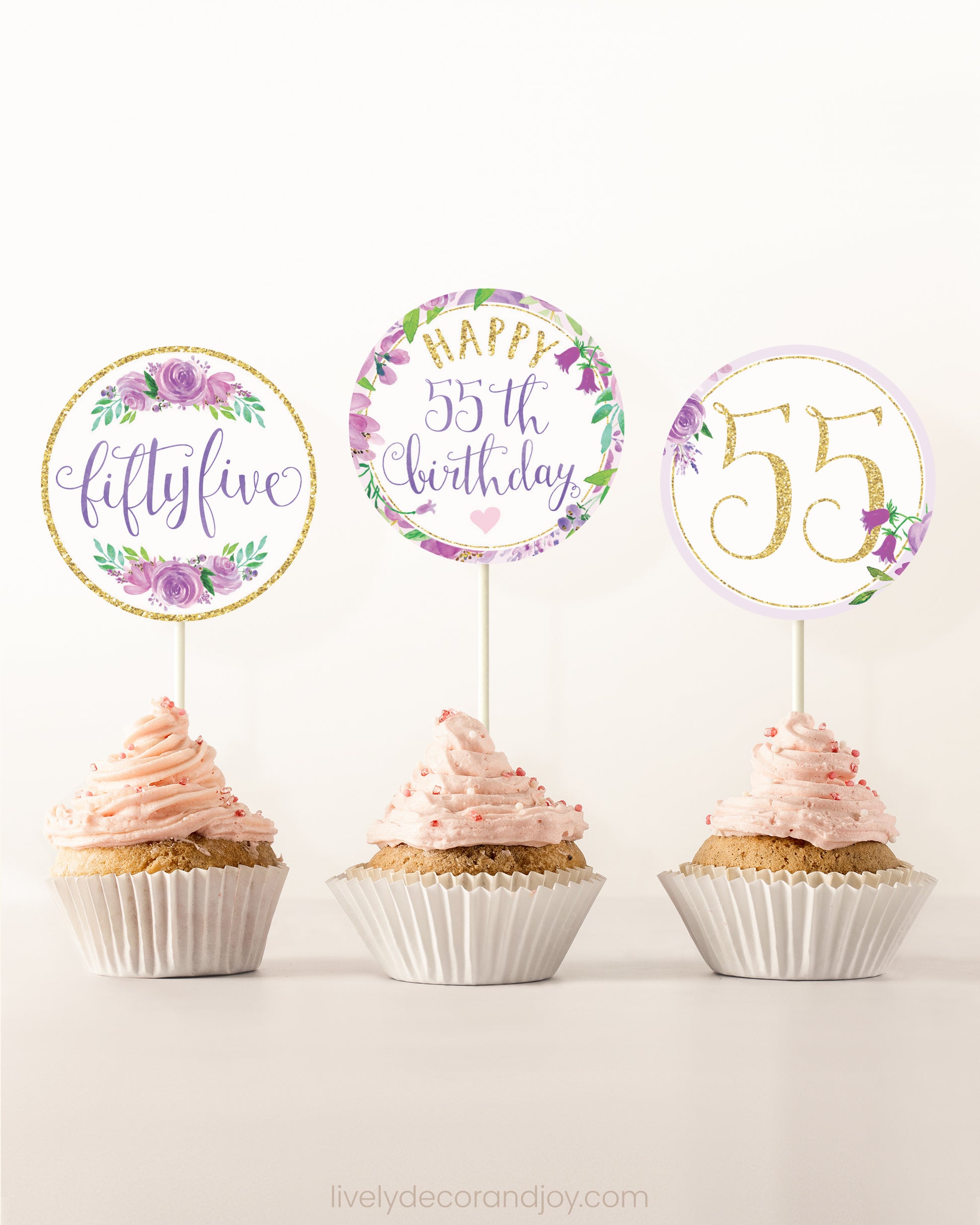 Three cupcakes on a dessert table. Each has a round cupcake topper with purple watercolor floral designs and purple and gold letters.