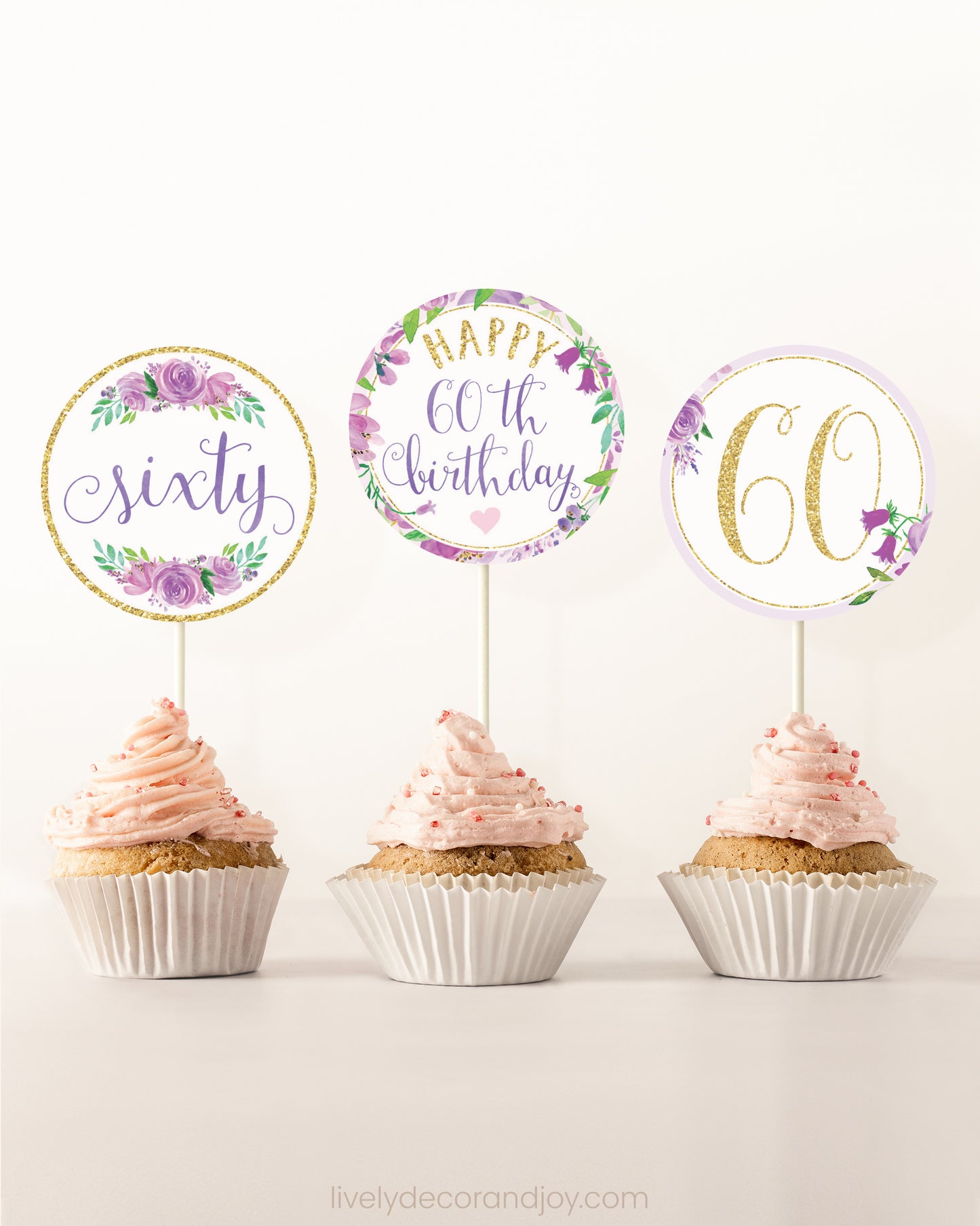 Three cupcakes side by side. Each has a round cupcake topper with purple watercolor flowers and purple and gold letters.