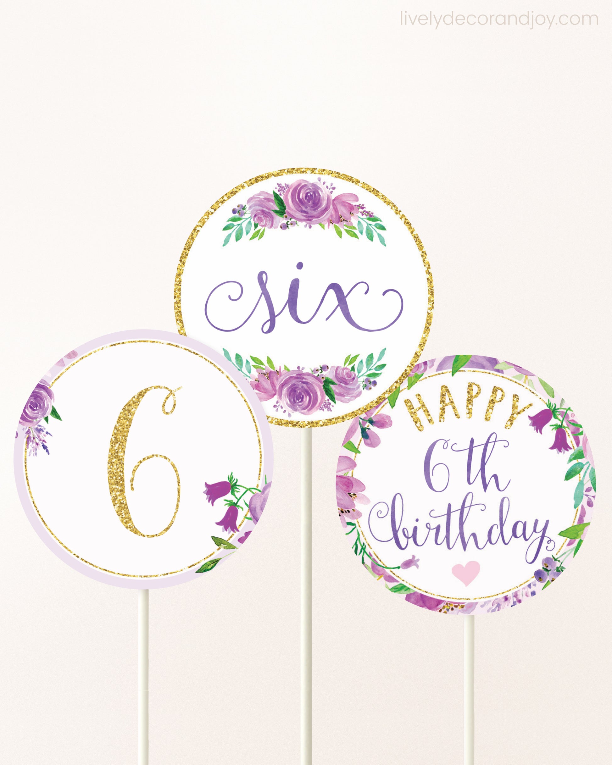 Three cupcakes toppers attached to lollipop sticks. They feature purple watercolor floral designs and purple and gold handwritten text.