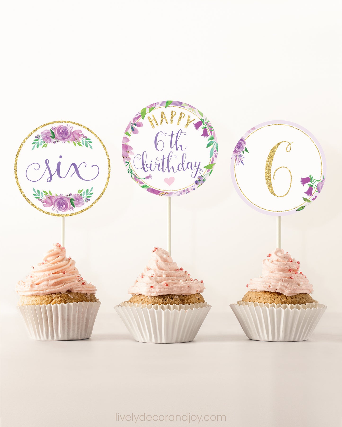 Three cupcakes on a dessert table. Each has a round cupcake topper with purple watercolor floral designs and purple and gold letters.