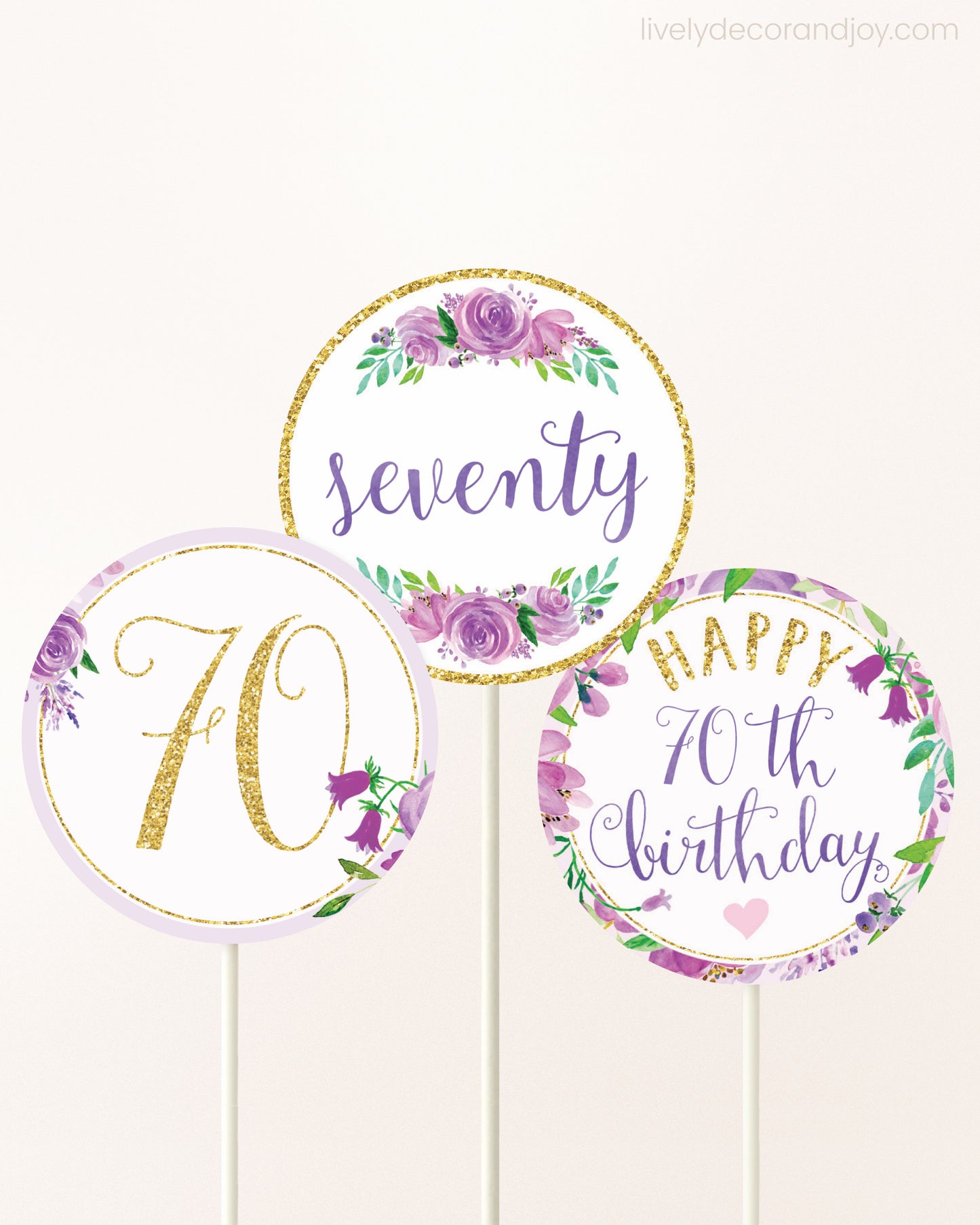 Three cupcakes toppers attached to lollipop sticks. They feature purple watercolor floral designs and purple and gold handwritten text.