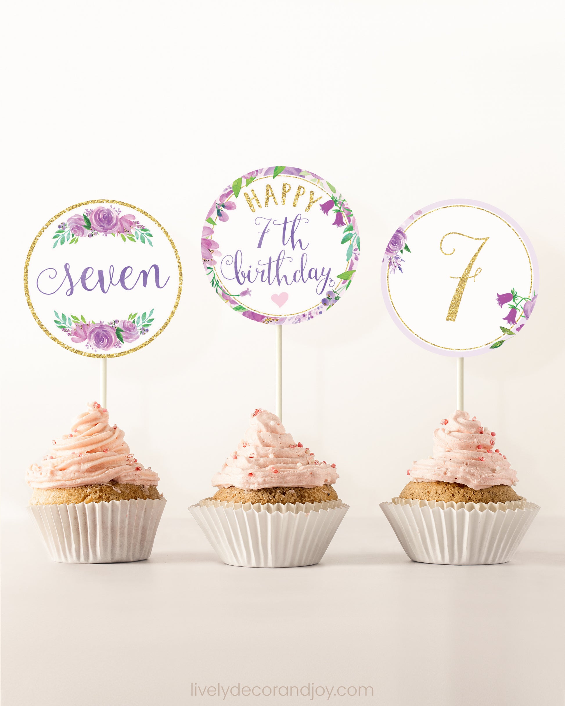 Three cupcakes side by side. Each has a round cupcake topper with purple watercolor flowers and purple and gold letters.