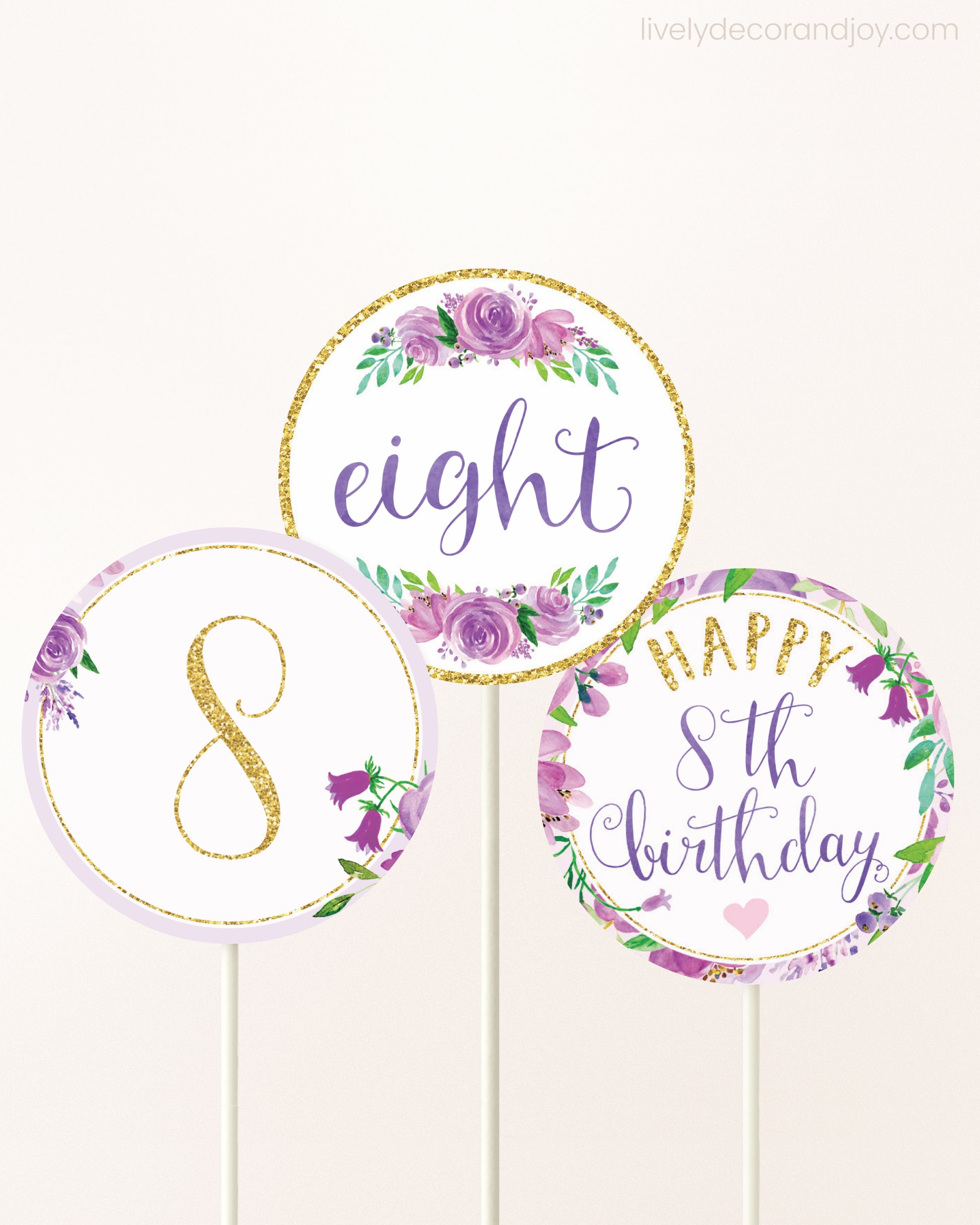 Three cupcakes toppers attached to lollipop sticks. They feature purple watercolor floral designs and purple and gold handwritten text.