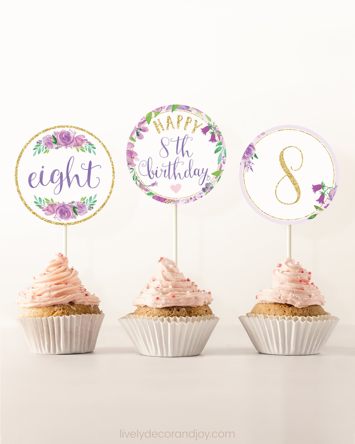 Three cupcakes on a dessert table. Each has a round cupcake topper with purple watercolor floral designs and purple and gold letters.