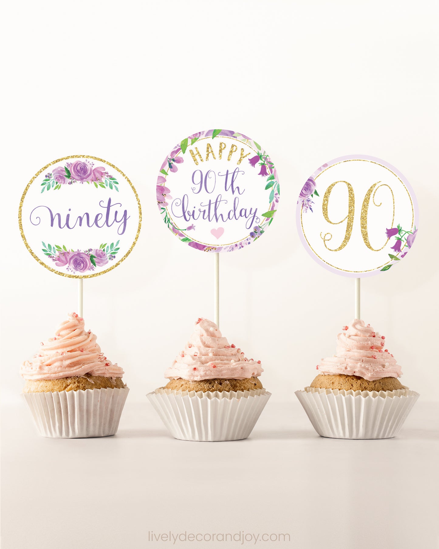 Three cupcakes side by side. Each has a round cupcake topper with purple watercolor flowers and purple and gold letters.