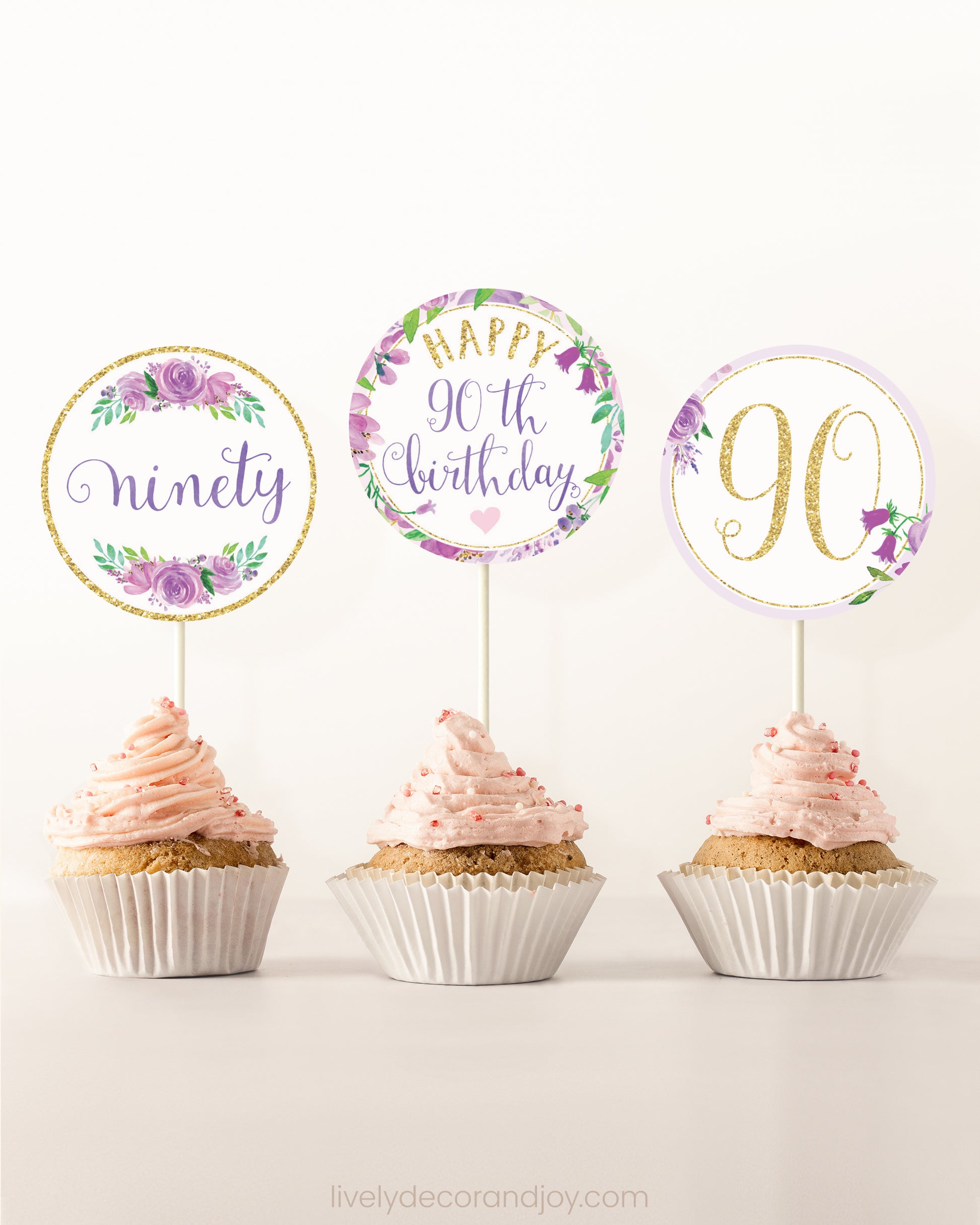 Three cupcakes side by side. Each has a round cupcake topper with purple watercolor flowers and purple and gold letters.