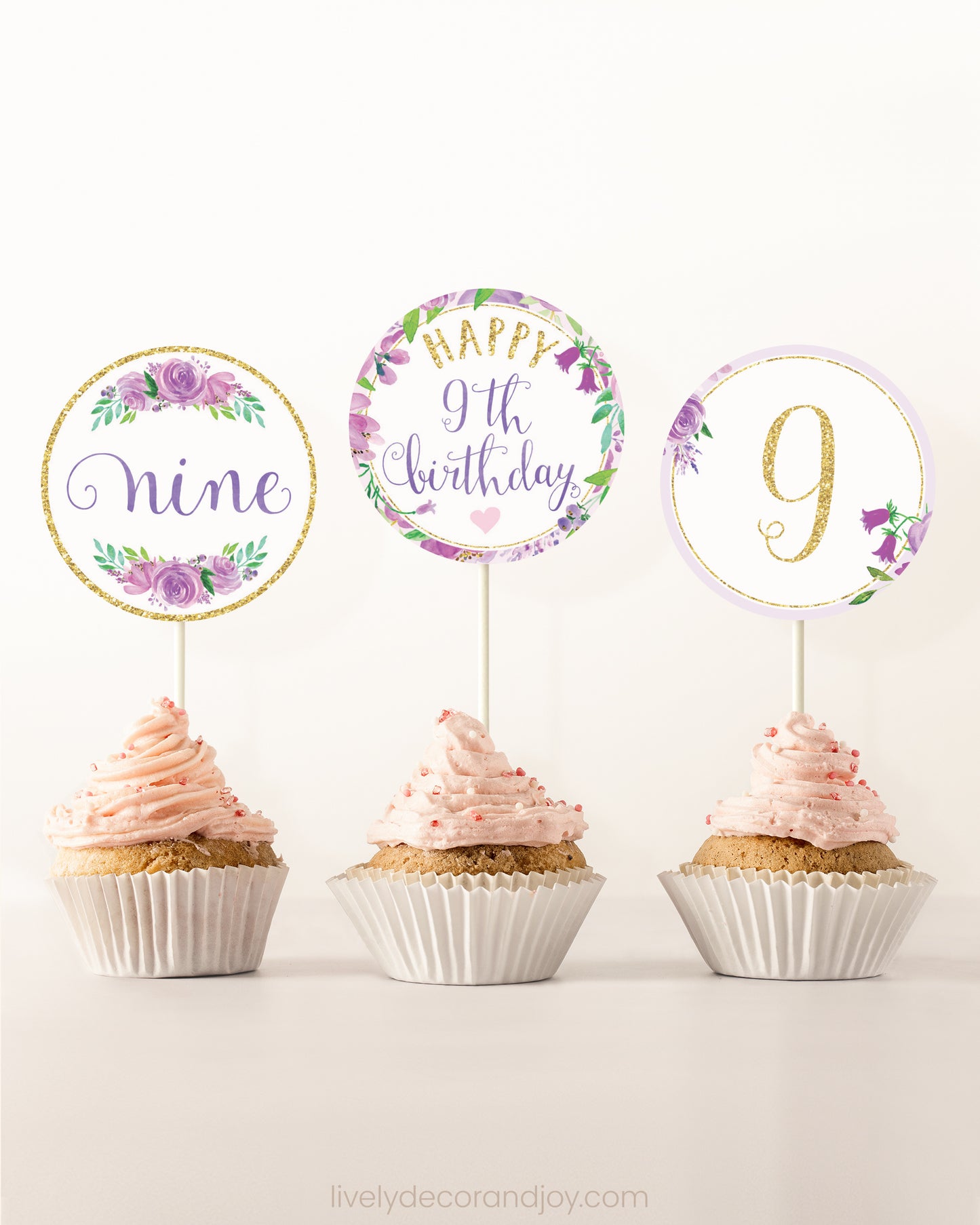 Three cupcakes side by side. Each has a round cupcake topper with purple watercolor flowers and purple and gold letters.